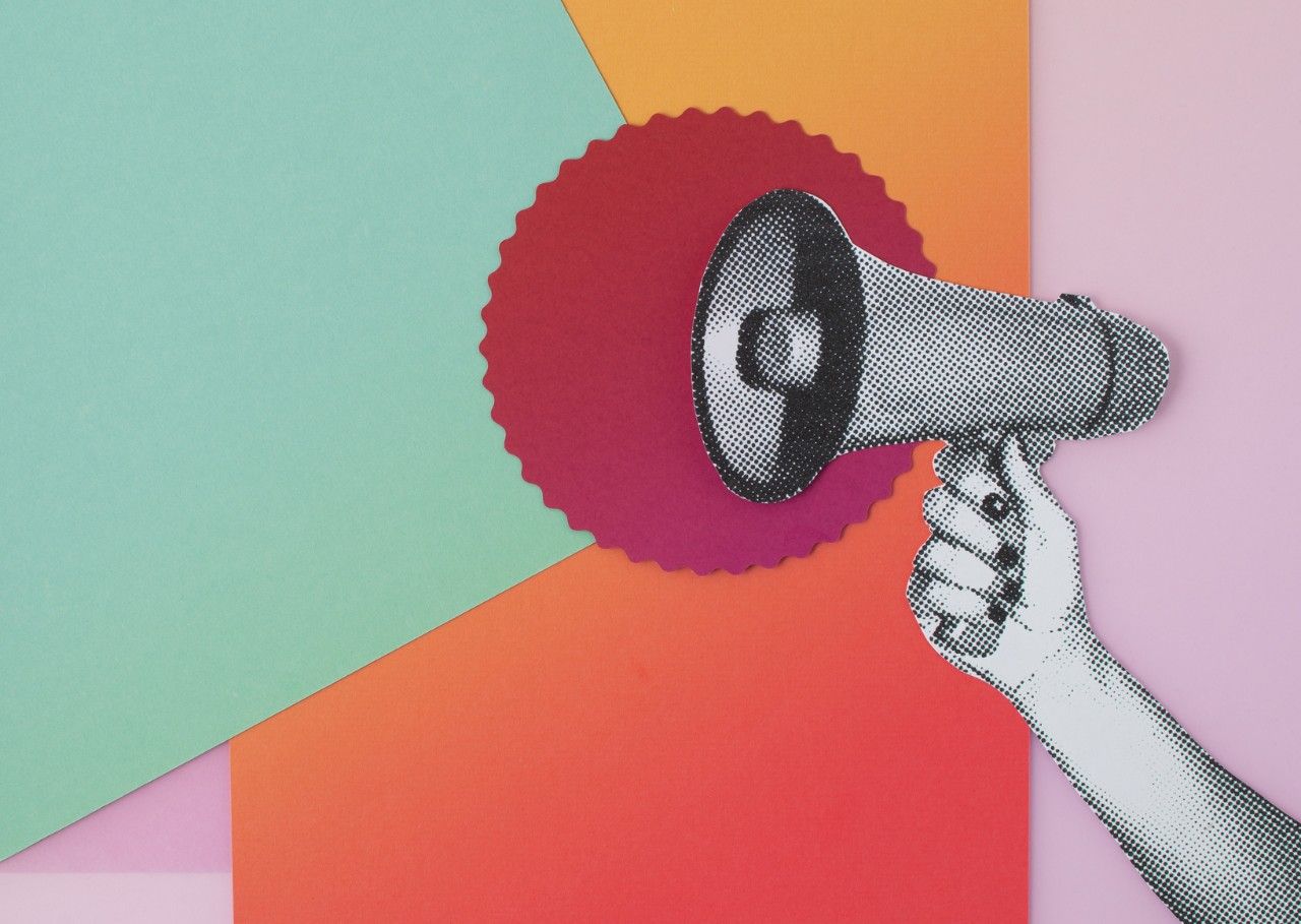 A pop-art style hand holding a megaphone in front of an abstract, colour-block background.