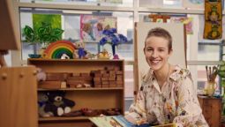 Certificate III in Early Childhood Education and Care student Catrina smiling proudly in a classroom with toys and child's drawings in the background.