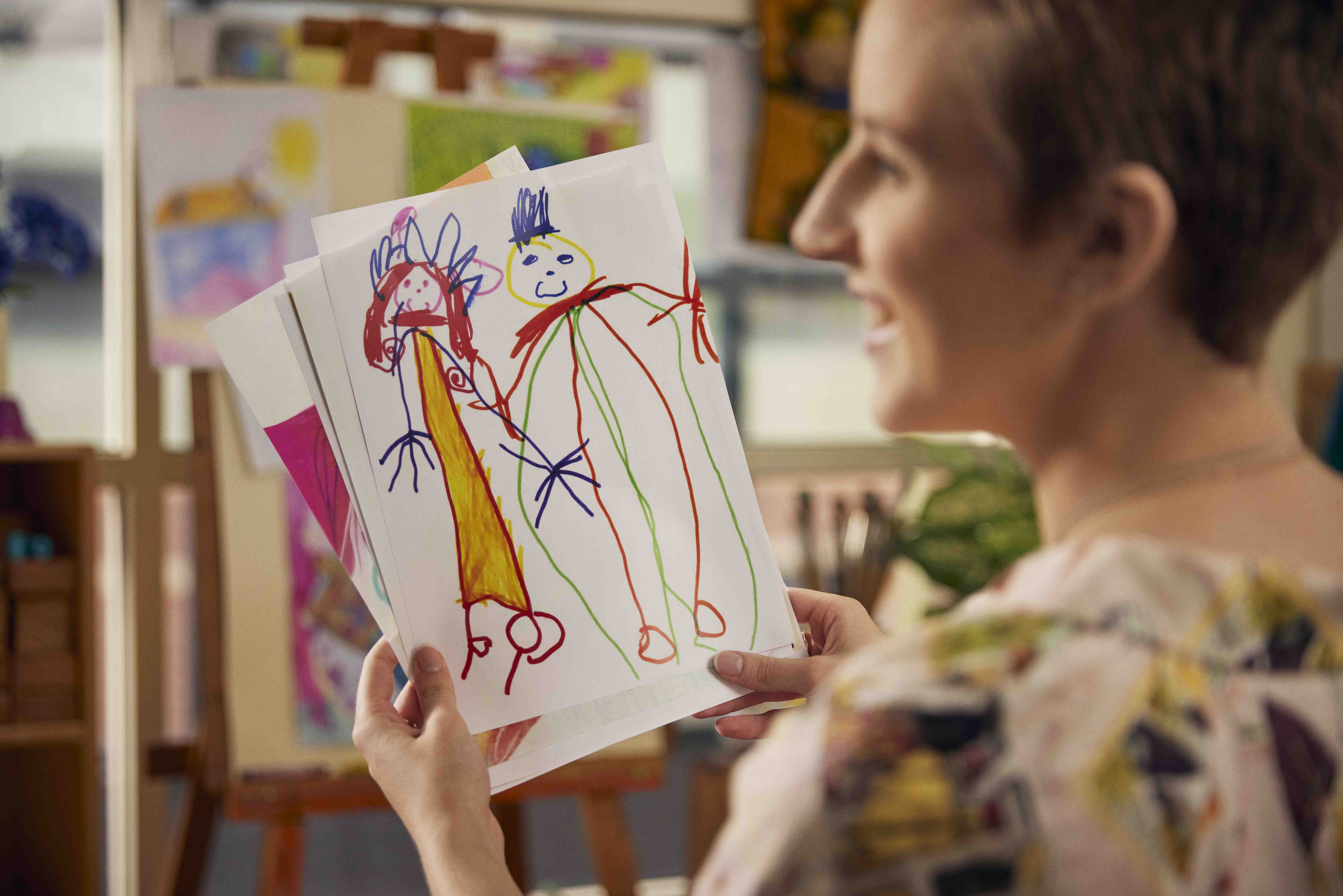 A student studying to be a teacher holding a child's drawing in a classroom