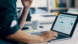 Adult working on a laptop with a report on the screen.