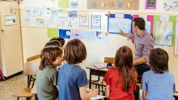A male teacher explaining the world map to a group of primary students