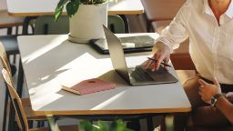 Student in a white shirt working on a laptop on a grey table.