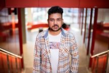 Abdullah, Master of IT student, looking straight into the camera in a checkered shirt and white t-shirt