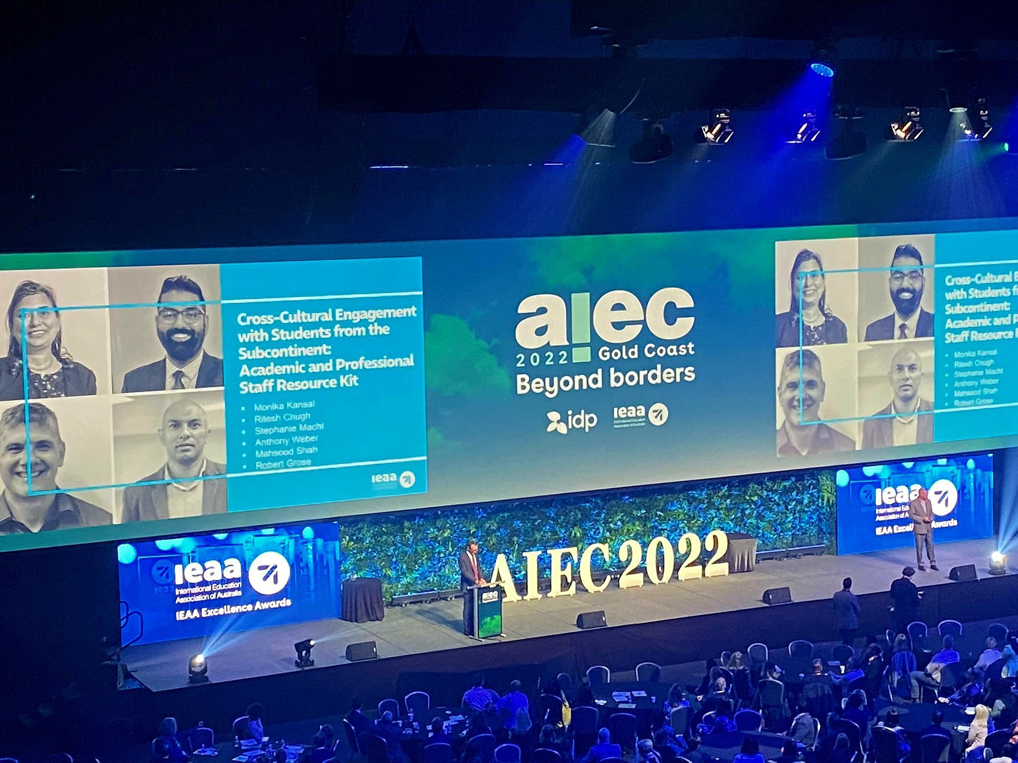 In a dark auditorium, Professor Shah's team and their project are introduced on the screen while the award is being presented. 