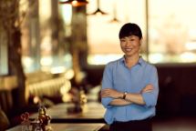 Confident Woman in Blue Shirt Smiling Inside Modern Restaurant