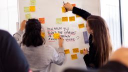Two females discussing and putting sticky notes on the white board.
