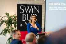Image of Belinda Collins speaking in front of an audience with a microphone. 