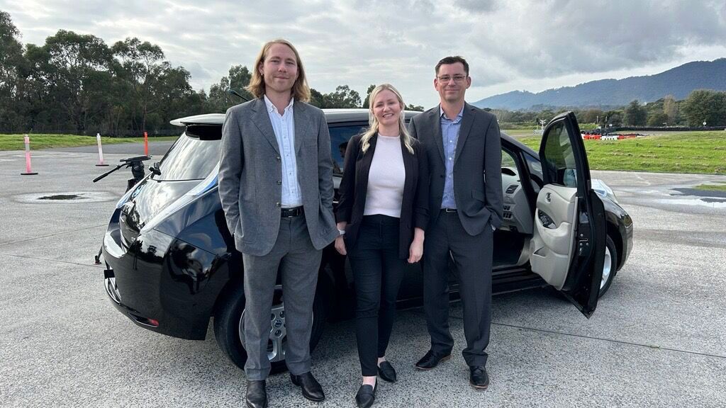 3 professional people standing in front of a car with the door open.