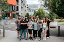 Ten young students standing together in the middle of a university street in summer.