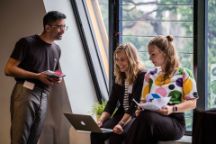 A male and two females discussing happily with a female holding laptop