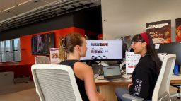 two people sitting at a table in front of a computer talking
