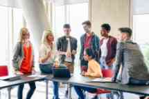 Six college students listening to female lecturer with laptop in classroom