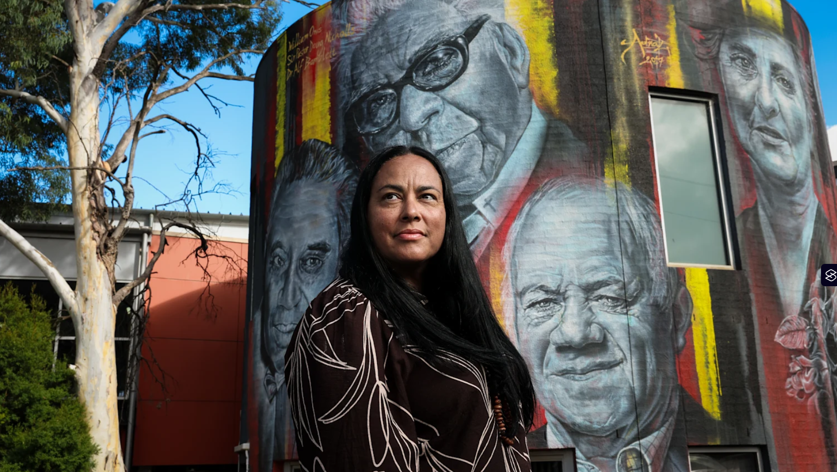 Woman standing outside in front of spraypainted wall with iconic figures