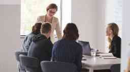 Office workers in a business meeting room around a table. 
