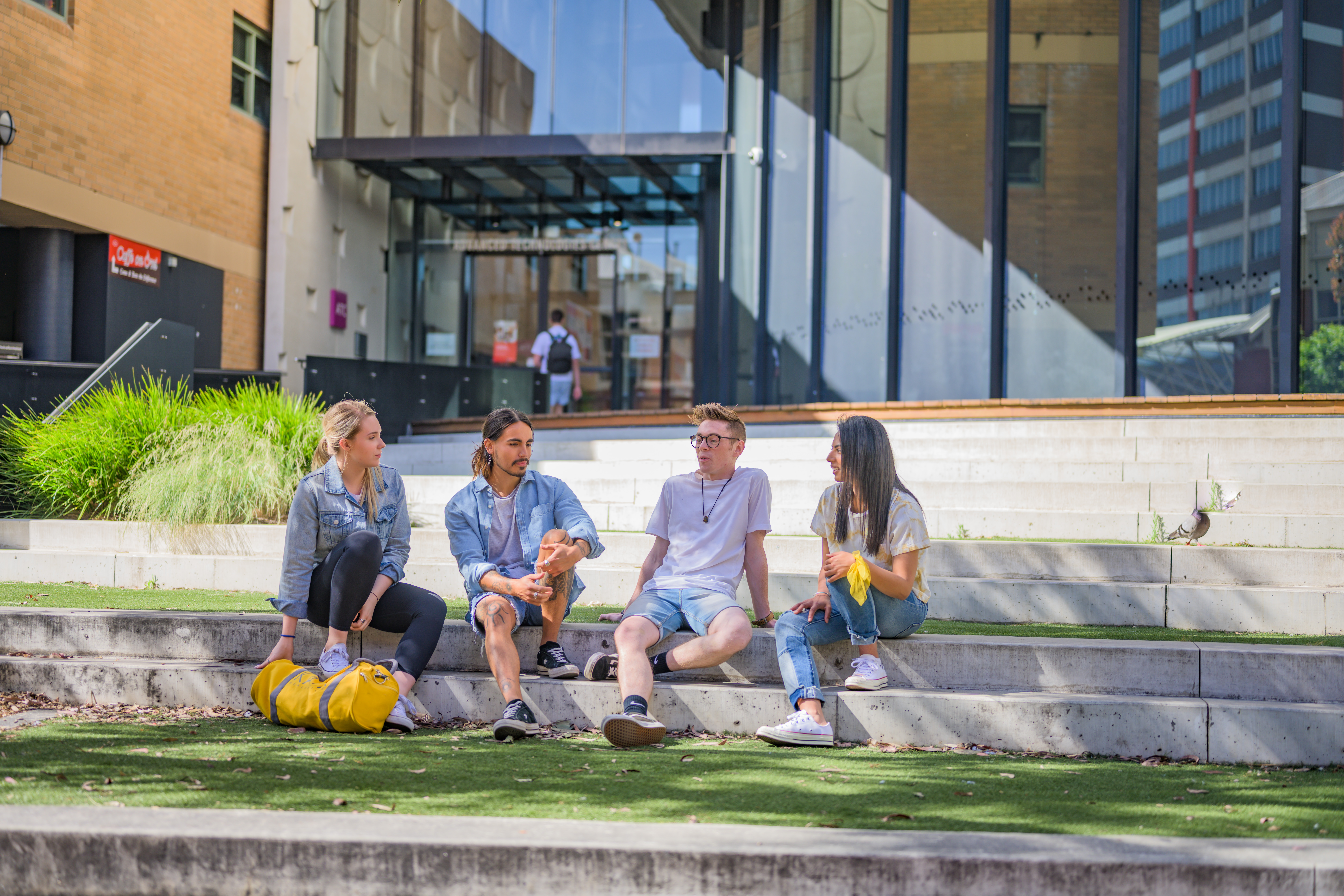 Group of 4 students sitting and chatting on the roman stairs out the front of ATC