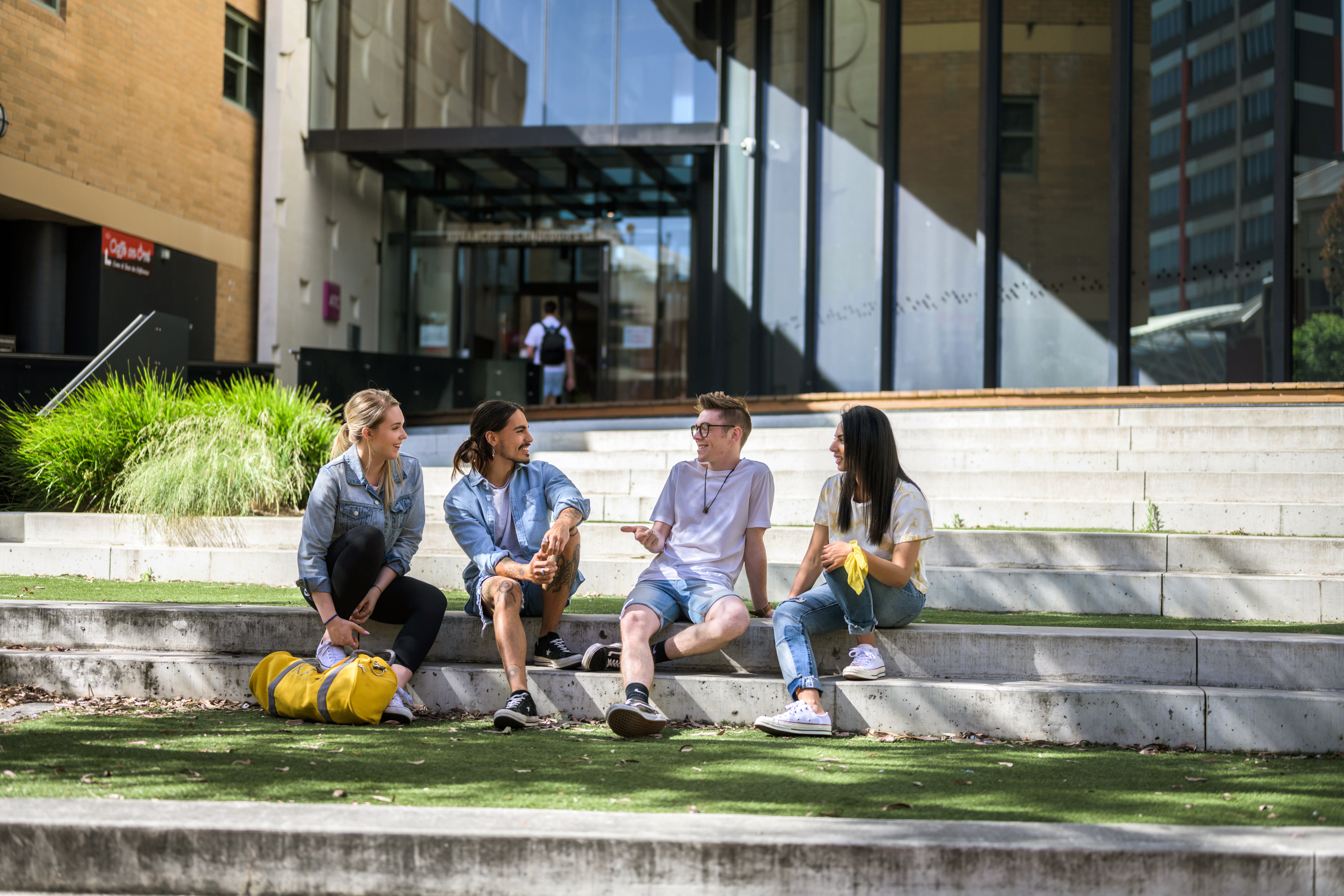Group of 4 students sitting and chatting on the roman stairs out the front of ATC