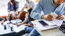 Young male writing notes on paper at desk. 
