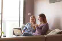 Two female students relax on a couch with a laptop open