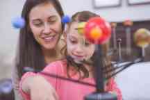 Mother and daughter learning about astronomy together using a model of planets and the solar system. 