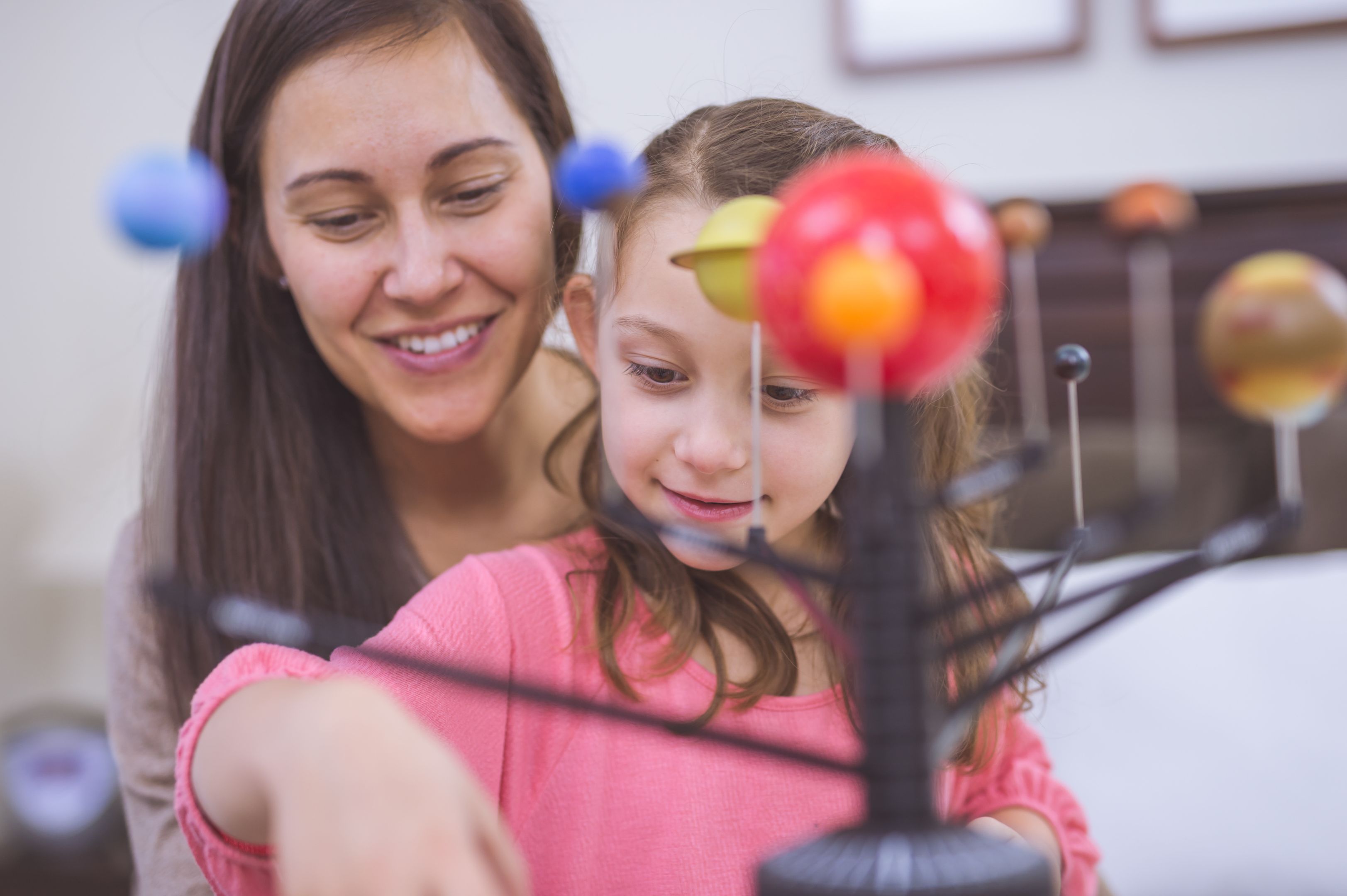 Mother and daughter learning about astronomy together using a model of planets and the solar system. 