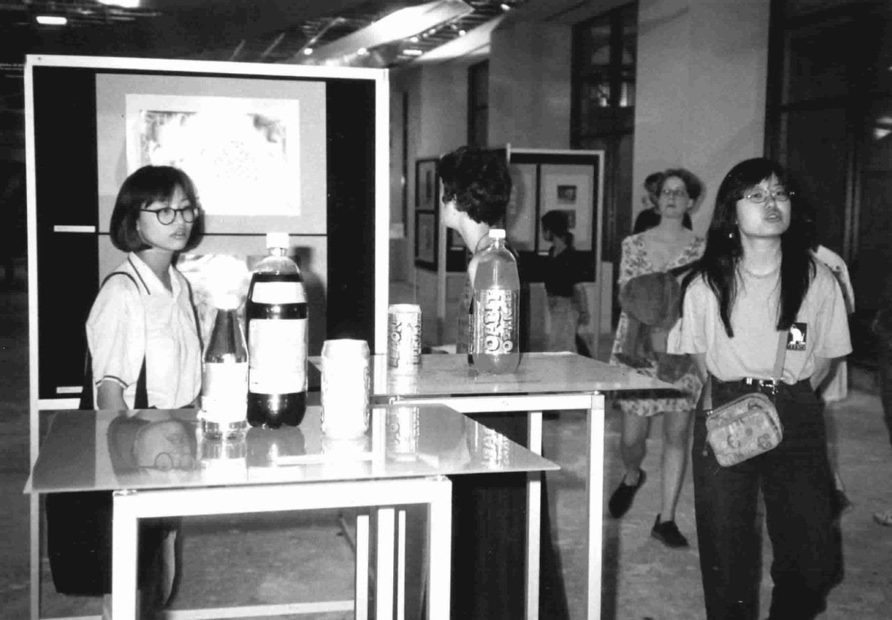 A group of six people walk around the Swinburne design exhibition. Artworks are displayed in pods scattered throughout the room. 