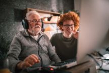 An elderly man and a young man watching a program together on a computer screen