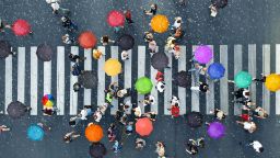 Aerial shot of pedestrians crossing the street carrying colourful umbrellas in the rain