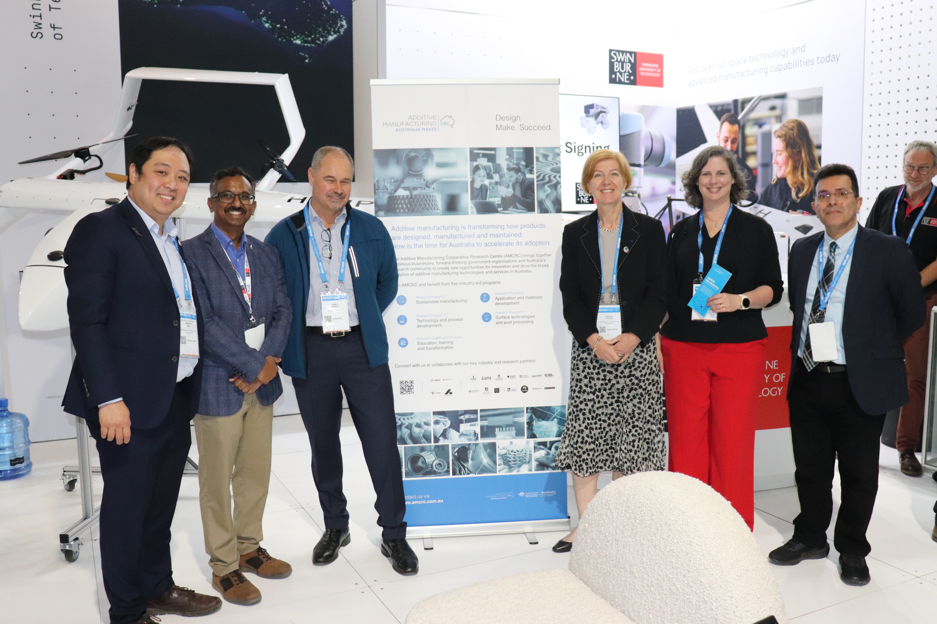 A group of six Swinburne leaders involved in the Additive Manufacturing Cooperative Research Centre stand next to a banner at the Avalon Airshow 2025.