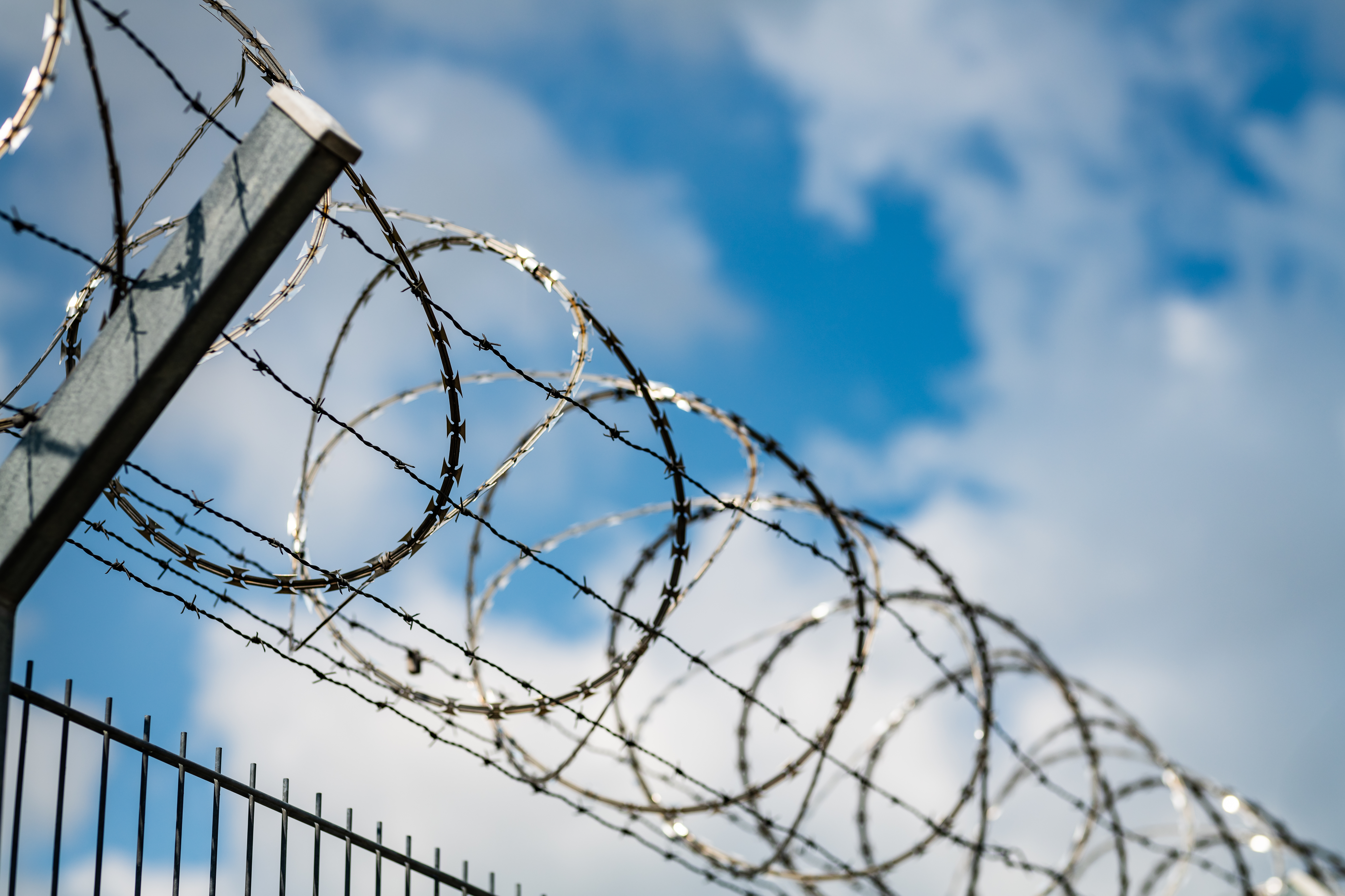 Barbed wire fence against blue sky with clouds