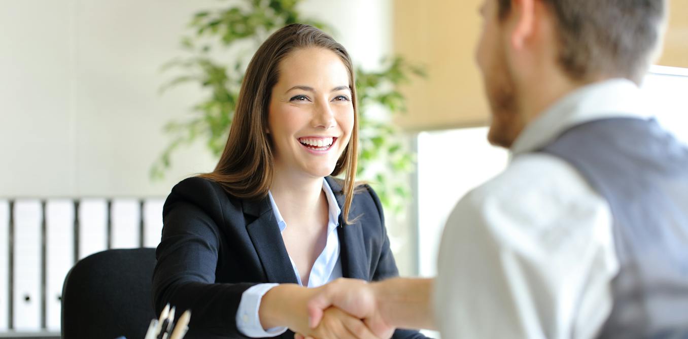 Two people shaking hands over a desk at a job interview
