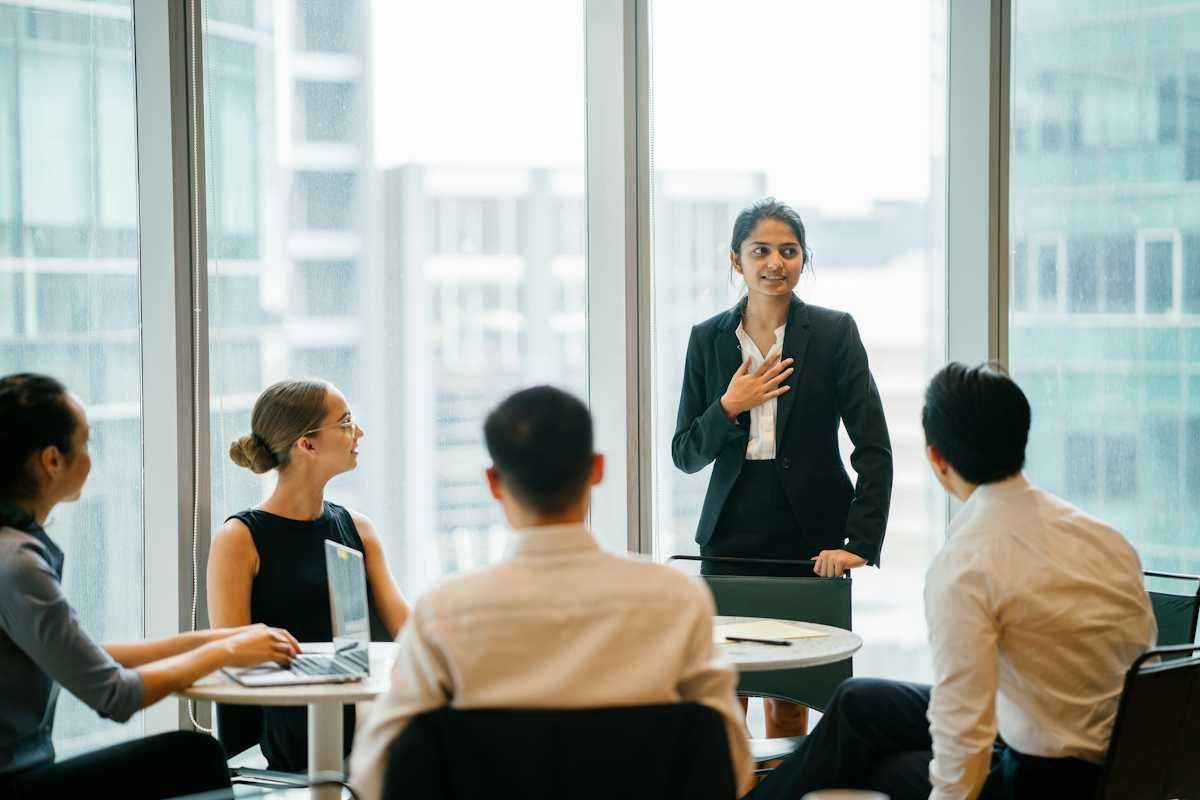 Women speaking at a business meeting with four people listening