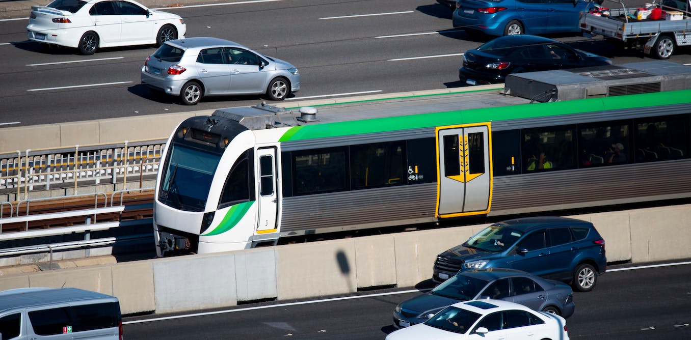 A freeway with cars driving and a train in the middle lane.