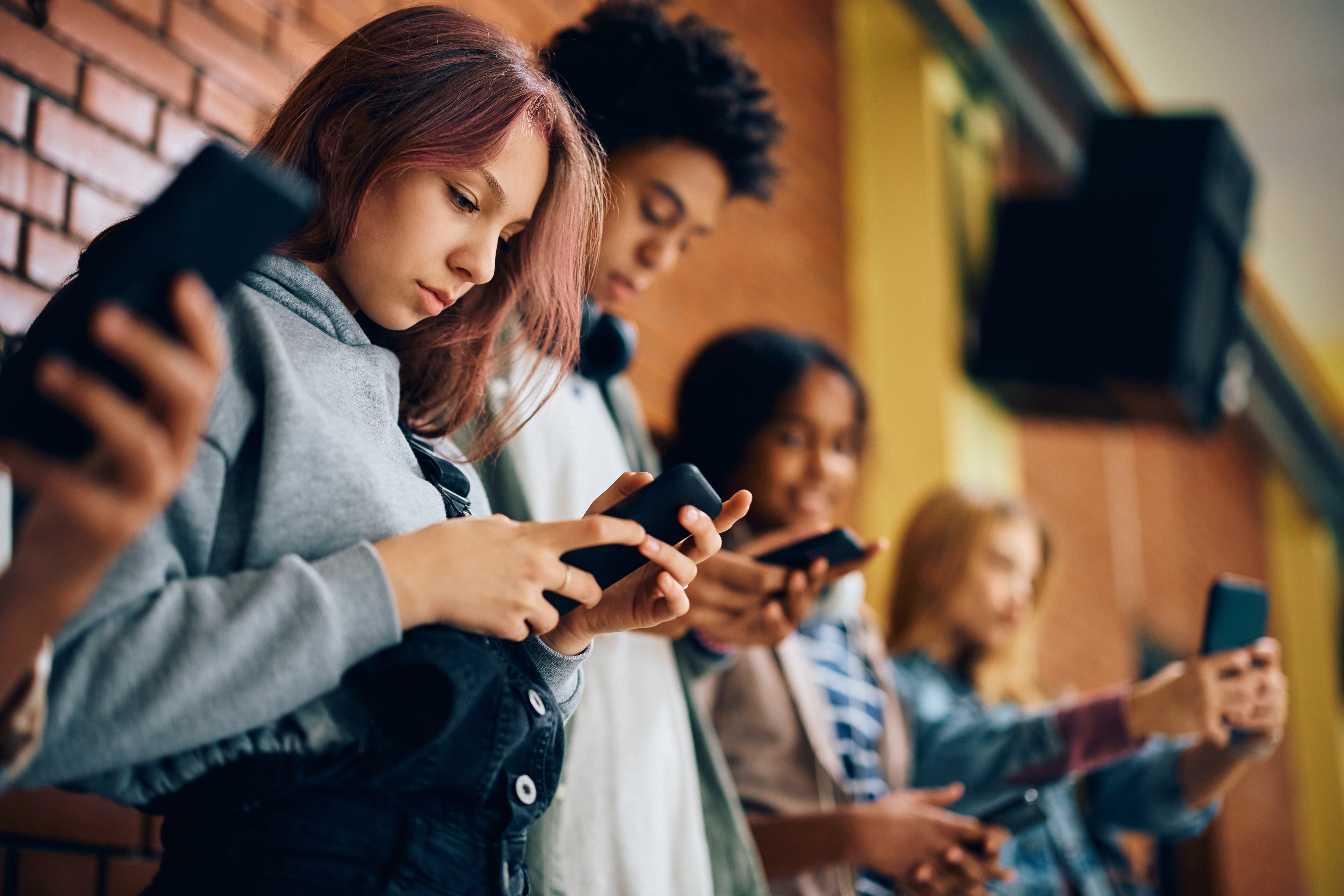 Group of teenagers using mobile phones in hallway at high school. 