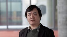 Man with short black hair brown jacket