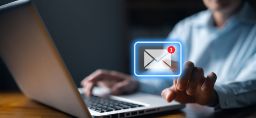 Man sitting at a laptop reaching out to touch a glowing new email icon floating above his computer screen. 