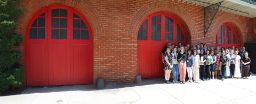 A group photo of the Education Innovation Exchange team members standing in front of a brick building with large red arched doors.