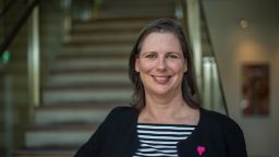 Karen has long hair and is looking at camera smiling. Karen wears a black blazer and a striped shirt.