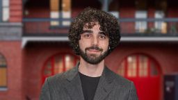 Young man with curly brown hair in professional attire, smiling at the camera.