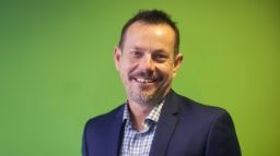 Nick Mills in a suit and with a green background