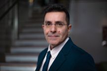 Man with glasses in a suit  standing slightly side on looking at the camera.