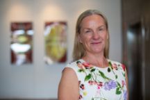 Laura-Anne Bull faces the camera smiling. Behind Laura-Anne is a triptych of artwork that is out of focus.