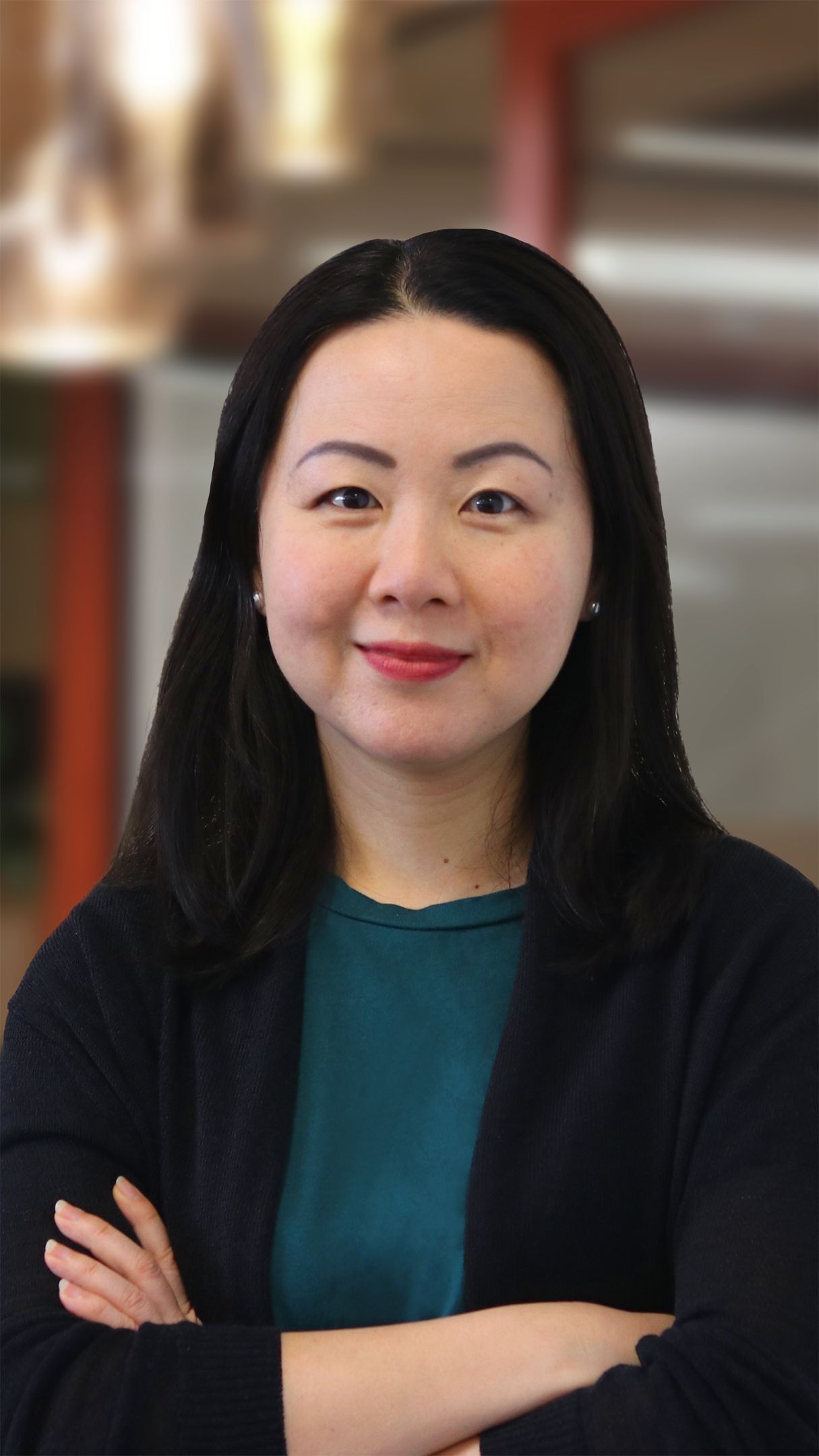Close up of a woman with long black hair, crossing her arms and smiling for the camera.