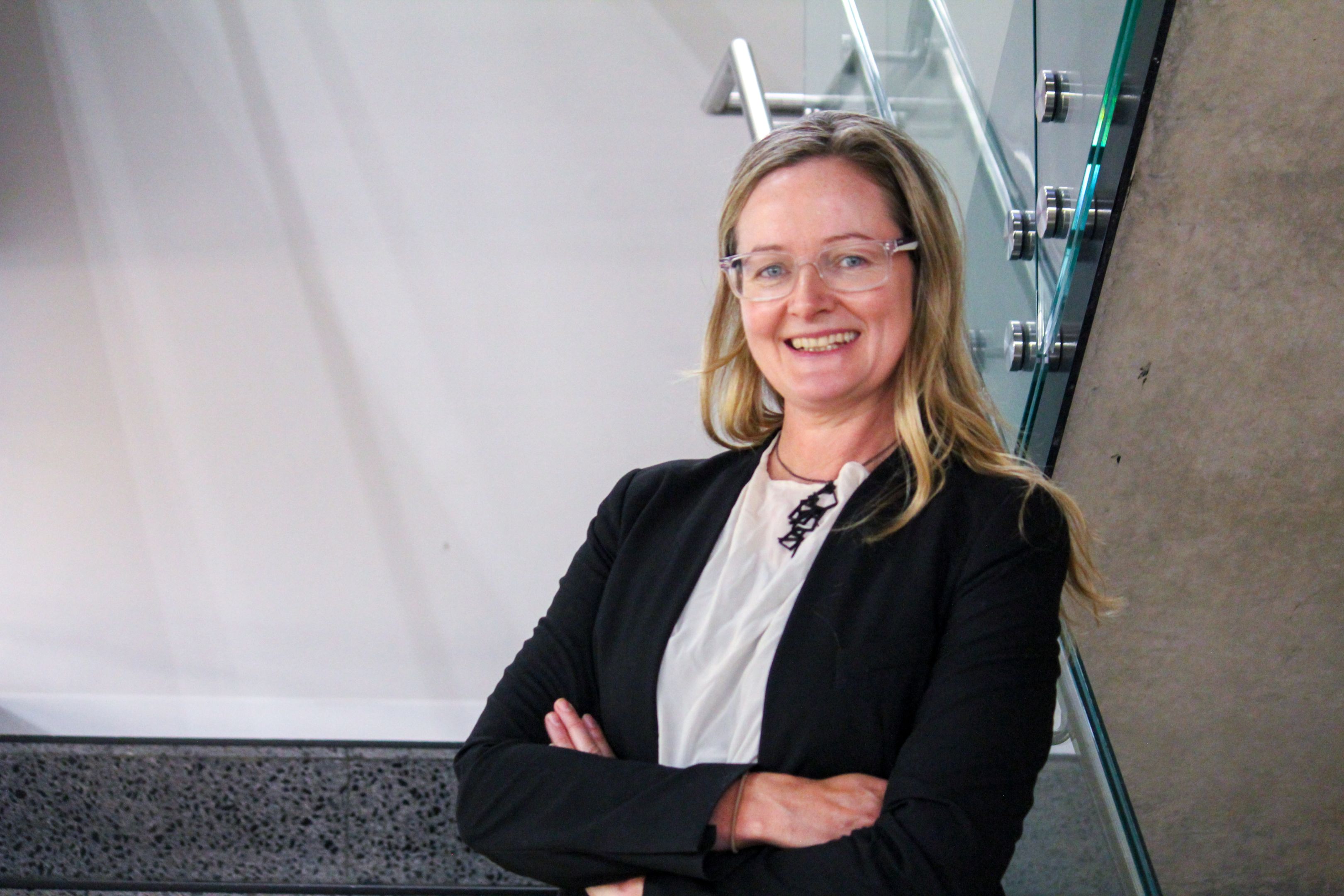 Swinburne Staff Member Ellen-Mary Terrill standing on a set of concrete stairs with a glass railing and a white wall behind. 