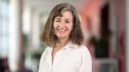 Professional looking woman in pink top facing the camera and smiling.