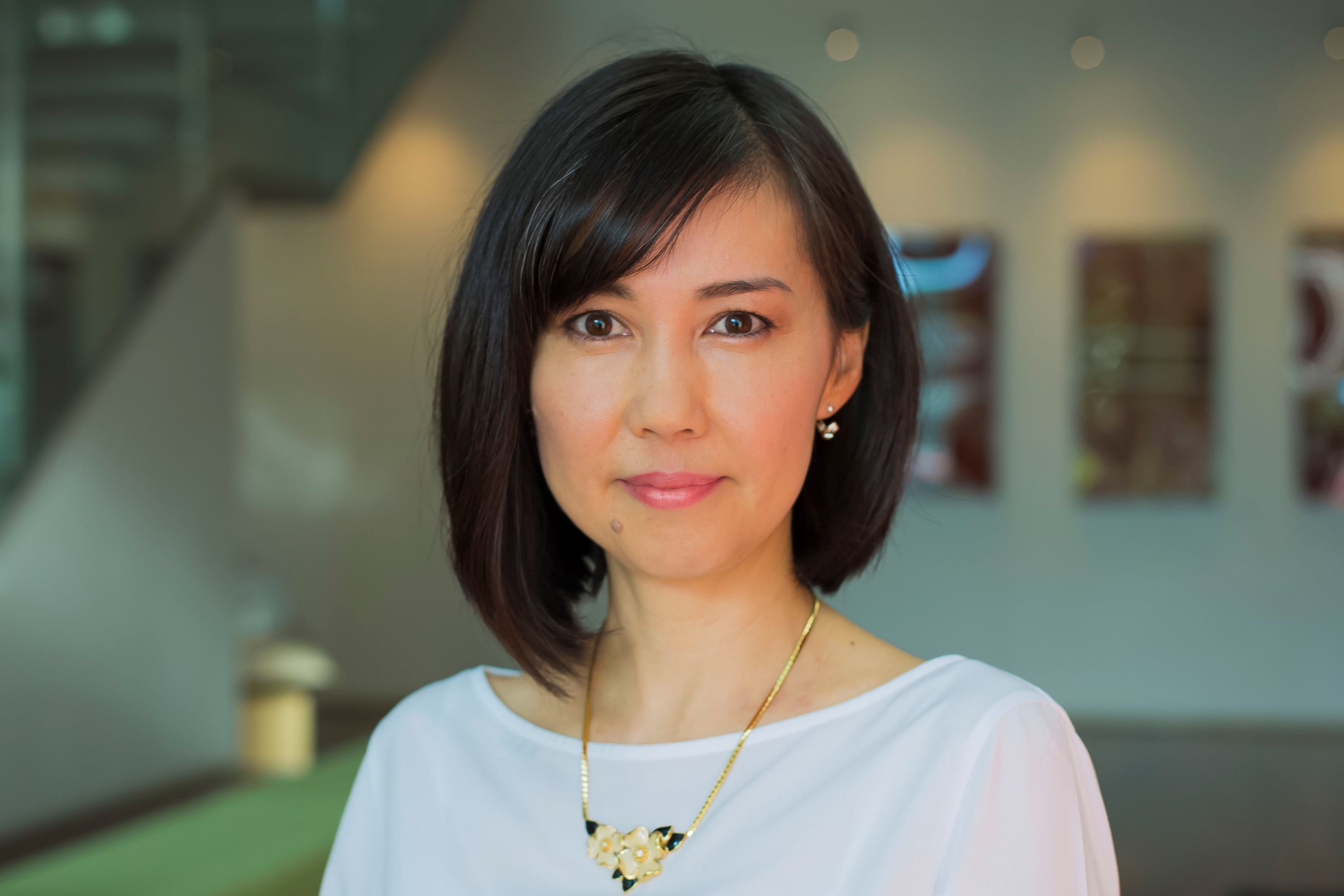 Yuki Kojima smiling wearing a white top in the foyer of the SPS building