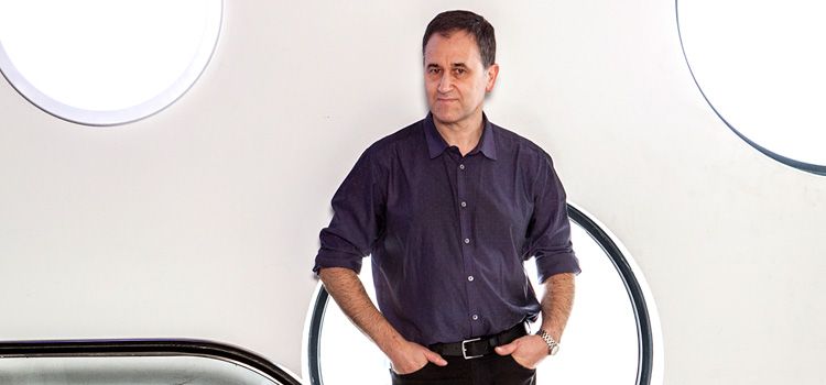 A man dressed in business casual clothes stands in front of a wall covered in large, circular windows