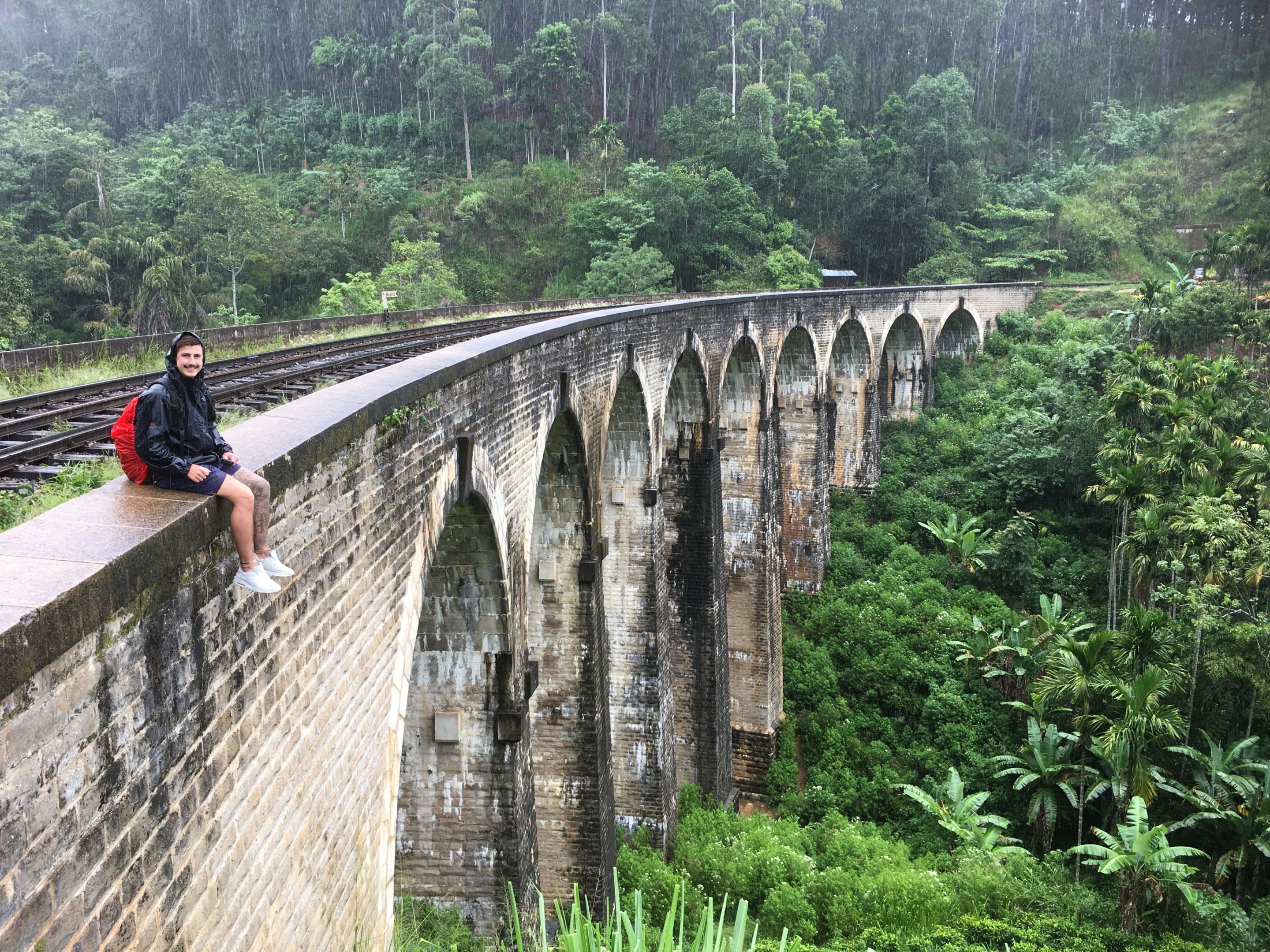 Man sitting on a old train bridge with a forest in the background
