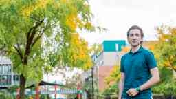 Young male student stands in a park smiling
