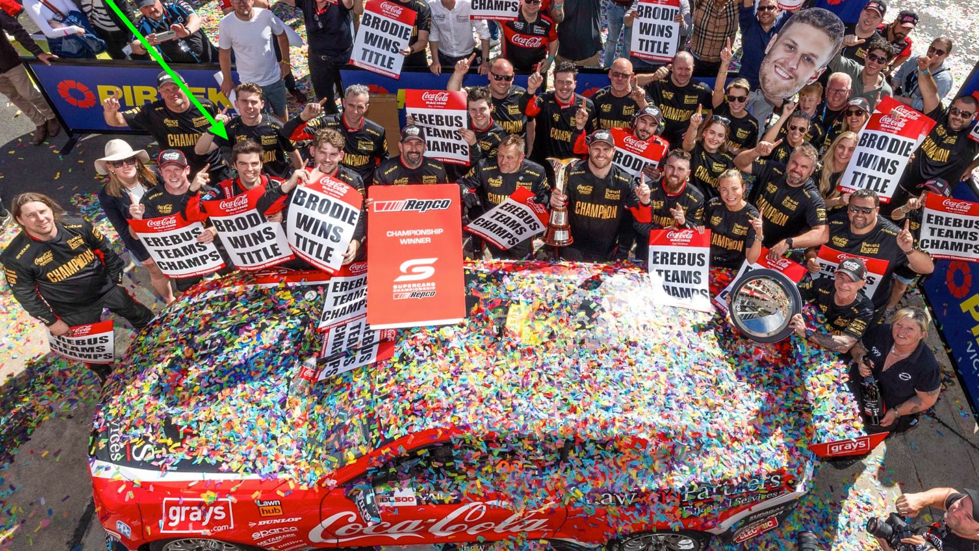 A crowd of supporters and the Erebus team with their championship winning car, covered in rainbow confetti.
