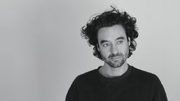 A black and white headshot of Kieran, in a black t-shirt and gazing off camera.